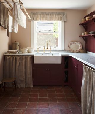 dark burgundy red utility room with a small window and farmhouse sink, under cabinet skirts and a dark terracotta floor