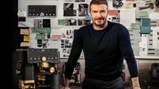 David Beckham stands in front of a large vision board, beside a black and gold coffee maker. 