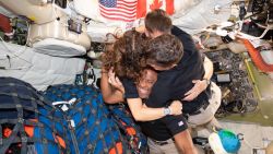 Four astronauts hug as they float in microgravity in a space capsule.