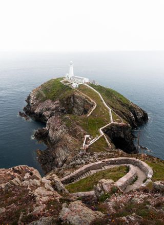 Photo of a winding path to a white lighthouse on a narrow piece of land jutting out to sea.