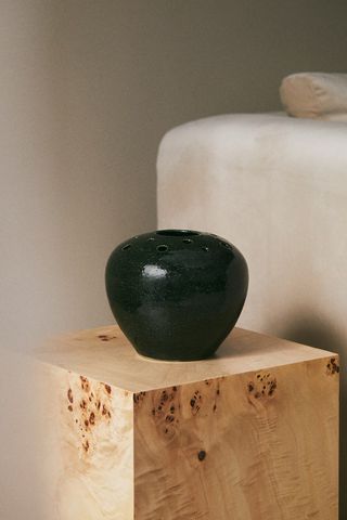 ikebana ceramic vase sitting on wooden plinth beside white sofa