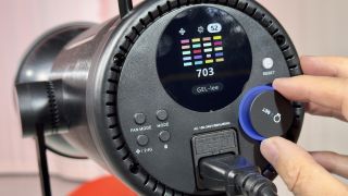 A hand adjusting the settings dial on the back of a Neewer CB200C COB RGB LED video light