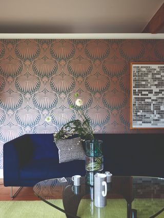 Damask brick red wallpaper in lounge with blue velvet couch and glass topped table