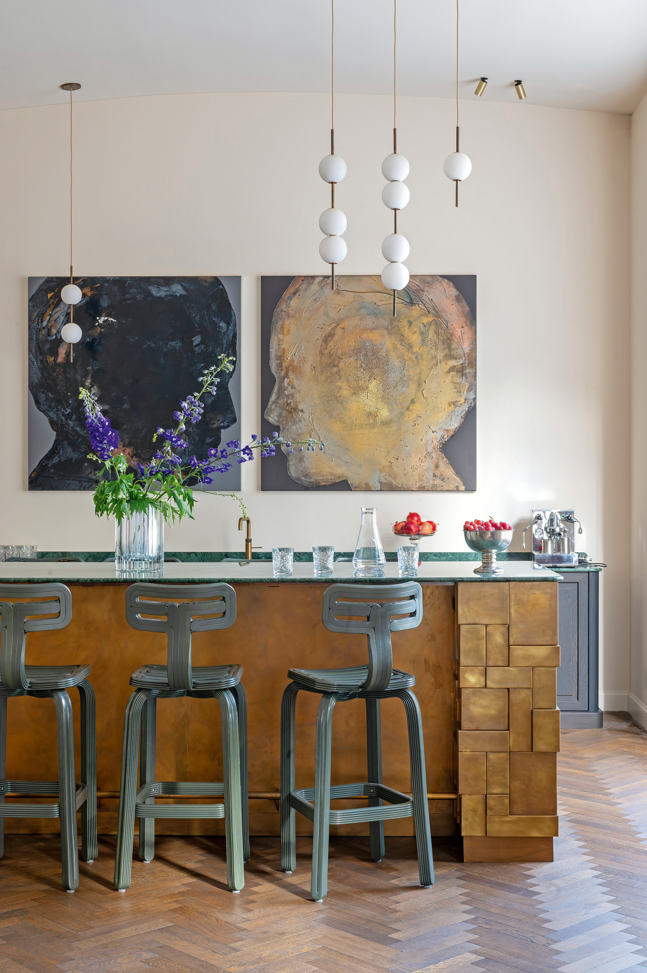 Kitchen with sculptural bronze island, steel blue bar stools, abstract portrait artwork and globe pendant lights
