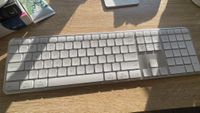 A silver grey Satechi Slim EX3 keyboard and Slim EX mouse on a wooden desk with sunlight shining on it from a window in the background