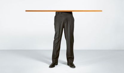 A mans legs with suit pants, smart shoes and with a piece of wood balancing on them.