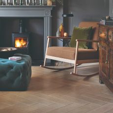 A dark grey-painted living room with a brown rocking chair, a fireplace and a teal ottoman