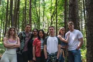 The Wreck season 2 cast stand in a forest, huddled together. From left to right: Alice Nokes as Sophia, Orlando Norman as Ben, Amber Grappy as Lauren, Thaddea Graham as Vivian, Oscar Kennedy as Jamie, Miya Ocego as Rosie, and Peter Claffey as Cormac