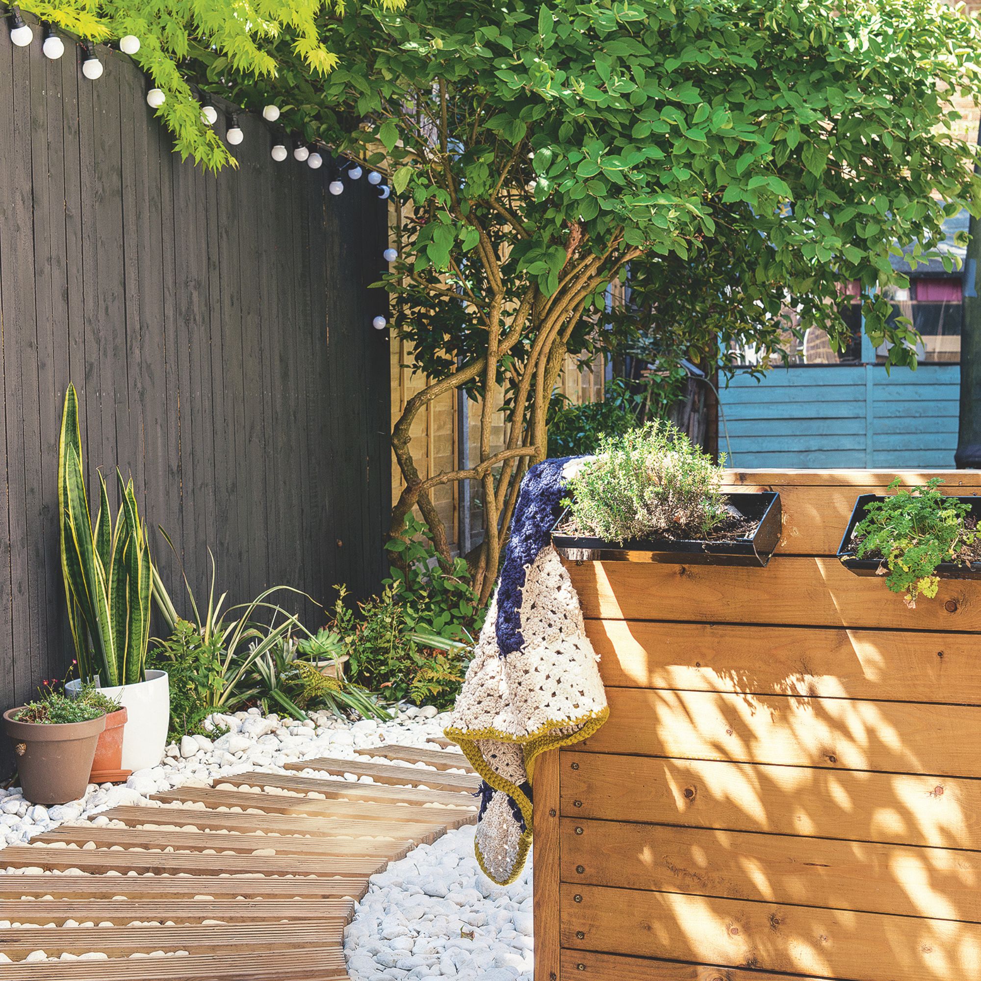 Garden area with a wooden path surrounded by white gravel, and plant pots underneath a black painted fence