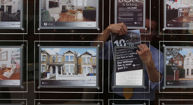 An estate agent employee hangs a promotional sign in the shop window