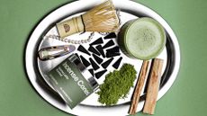 A silver tray with matcha latte incense cones, a bamboo whisk, a hair clip, a pearl string, wood sticks, and a glass of matcha