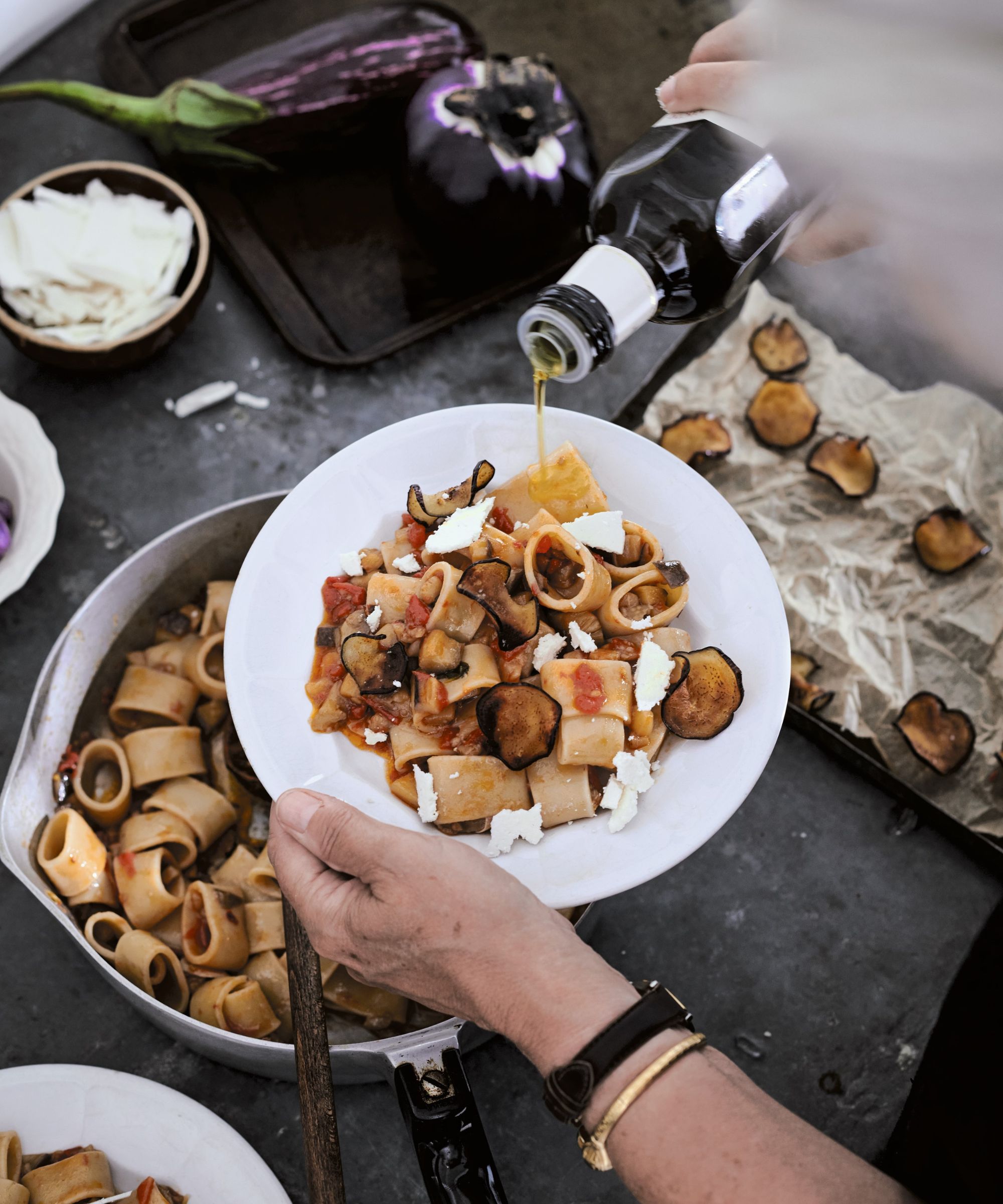 Serving pasta alla norma into a bowl with olive oil