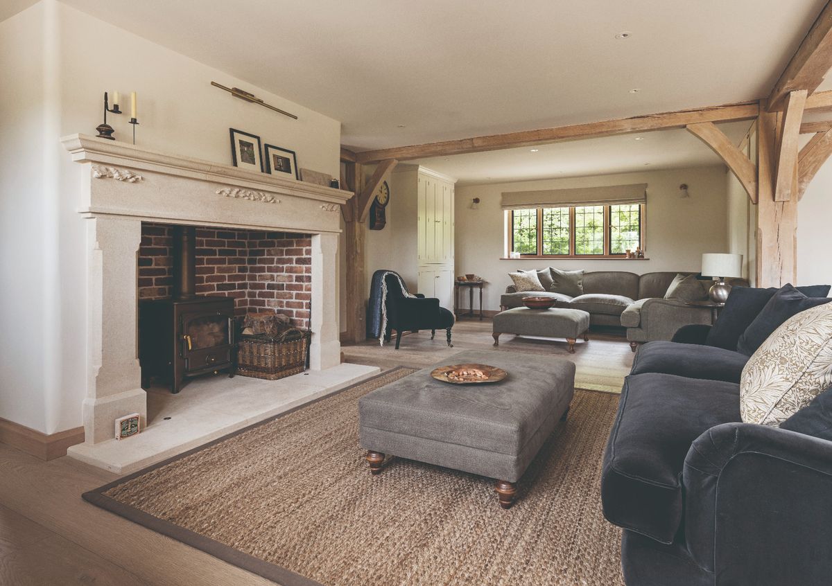 An open plan living room with a grand brick fireplace, a velvet sofa and an ottoman