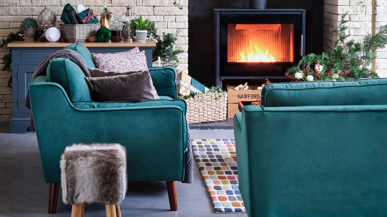 A living room with two emerald green velvet sofas and a wood burning stove decorated for Christmas