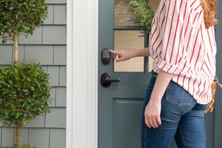 A woman in a striped shirt unlocking a Schlage Arrive Smart Wifi Deadbolt by pressing the buttons on the keypad