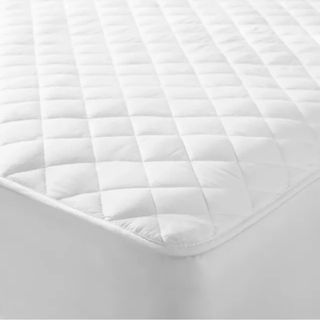 The corner of a white quilted mattress protector on a mattress