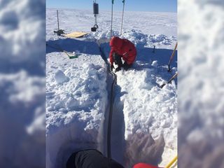 Researchers lay the conduit that connects the seismometer to the solar power system (background) and recording components at a Ross Ice Shelf seismic station.
