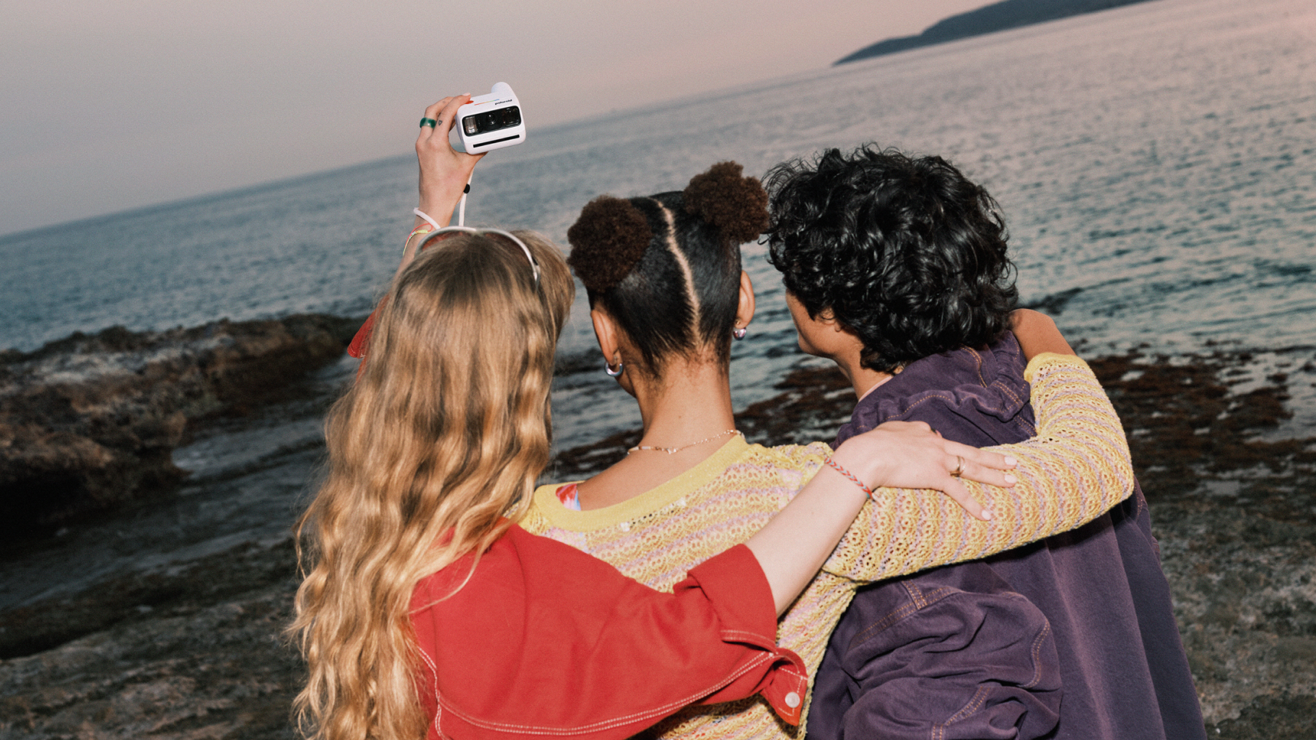 Three young people taking a selfie on the beach with the Polaroid Go Gen 3 - one girl is easily holding the tiny camera in one hand