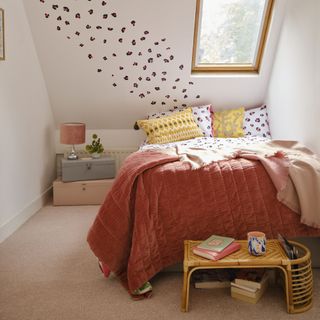 Neutral painted bedroom with bed with colourful bedding, bedside table