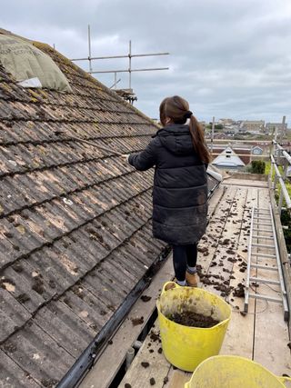 The roof tiles being cleaned by Ellie by using a wire brush to clean off the moss and stains whilst standing on a platform