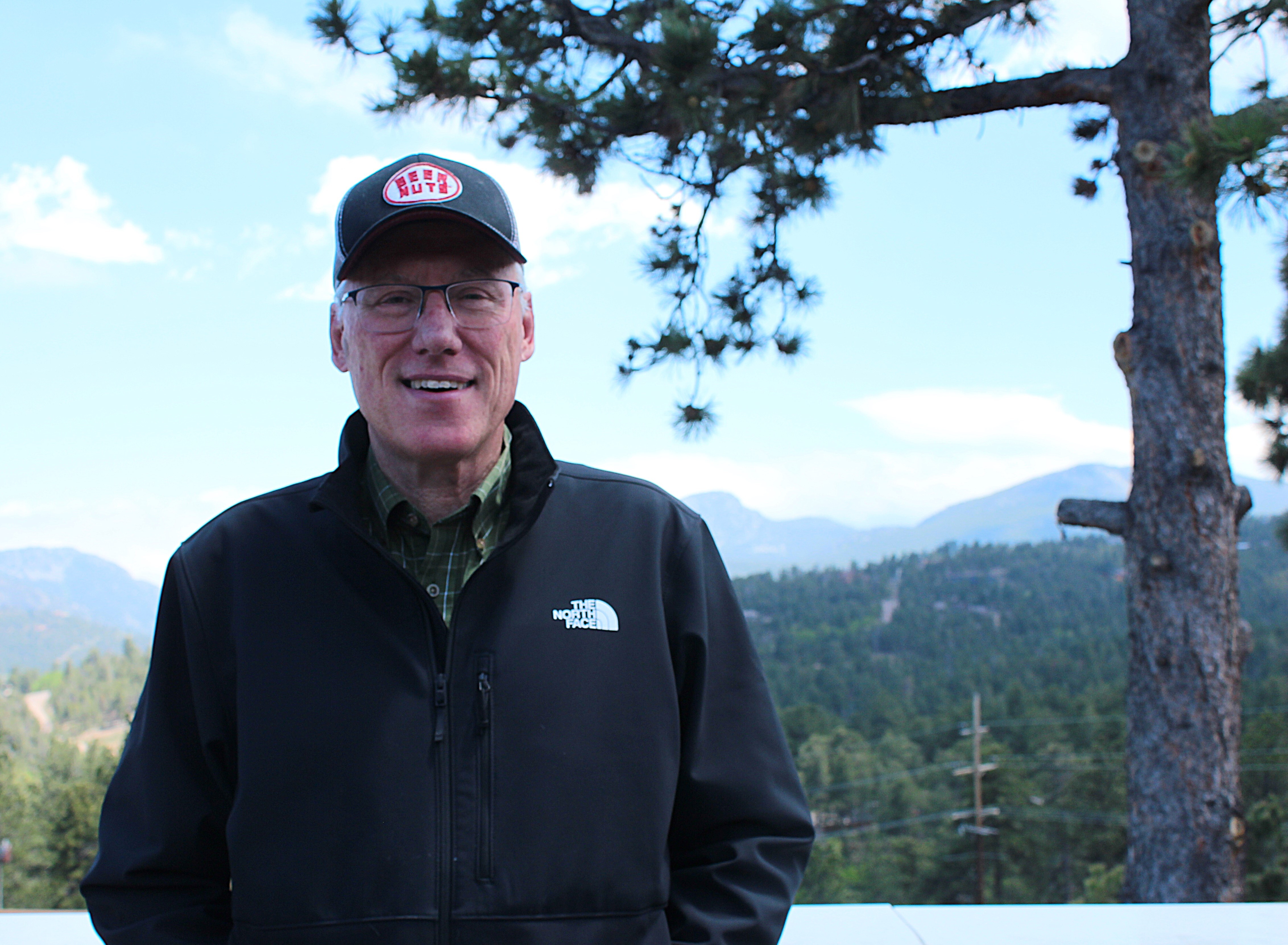 A man wearing a baseball hat and glasses looks at the camera.