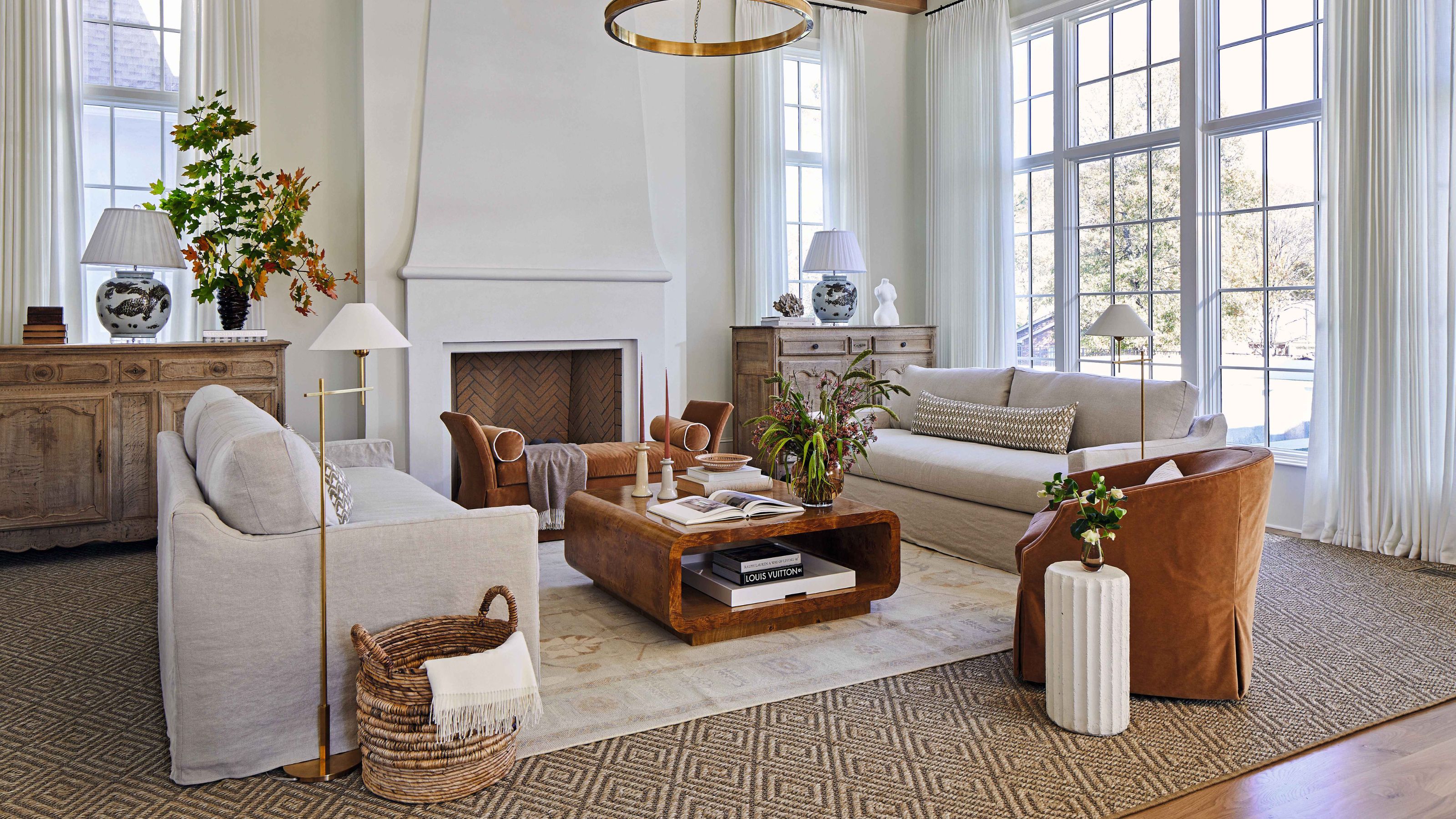 Large neutral living room with a soft color scheme. There is a large fireplace with two beige sofas, an linen orange armchair and a wooden coffee table