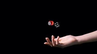A hand tosses a red die and a black die against a black background.