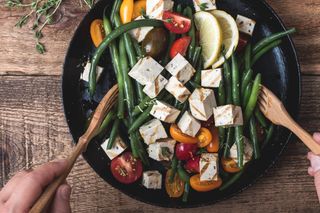 Delicious summer vegan meal, cooking healthy green beans salad with grilled tofu, fresh colorful mix cherry tomatoes, thyme herbs and lemon zest served in rural cast iron skillet, wooden forks, top view
