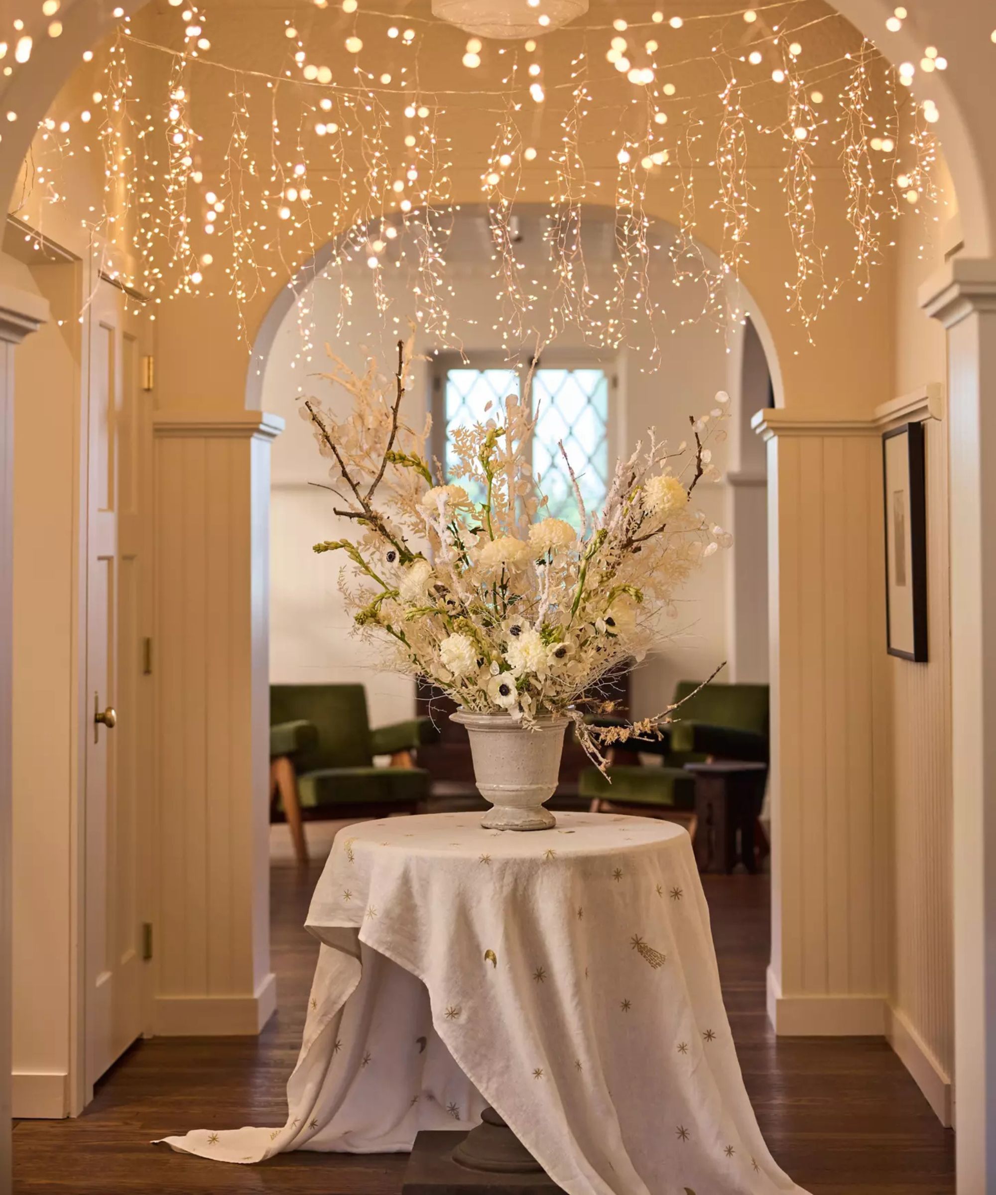 terrain arched neutral entryway with a round hall table, large white floral display in a vase with hanging fairy lights from the ceiling