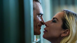 Arthur Fleck (Joaquin Phoenix) and Lee Quinzel (Lady Gaga) about to kiss through prison bars in &quot;Joker: Folie à Deux&quot;