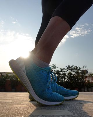 A close up of a person's feet in blue running shoes with the sun in the background