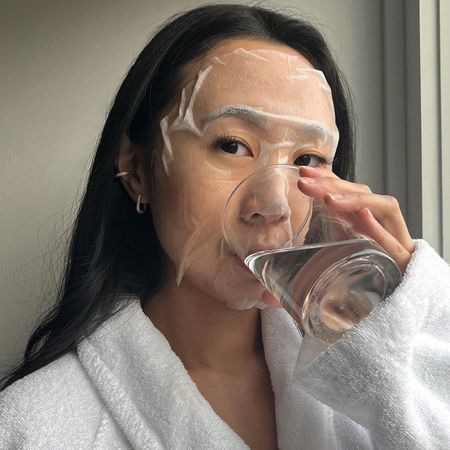 Woman wearing sheet mask and drinking water