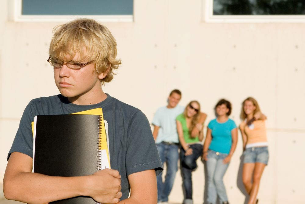 A teen boy stands apart from other students.