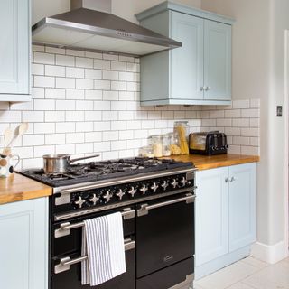 Kitchen with pale blue cabinetry and white metro tile splashback behind range cooker