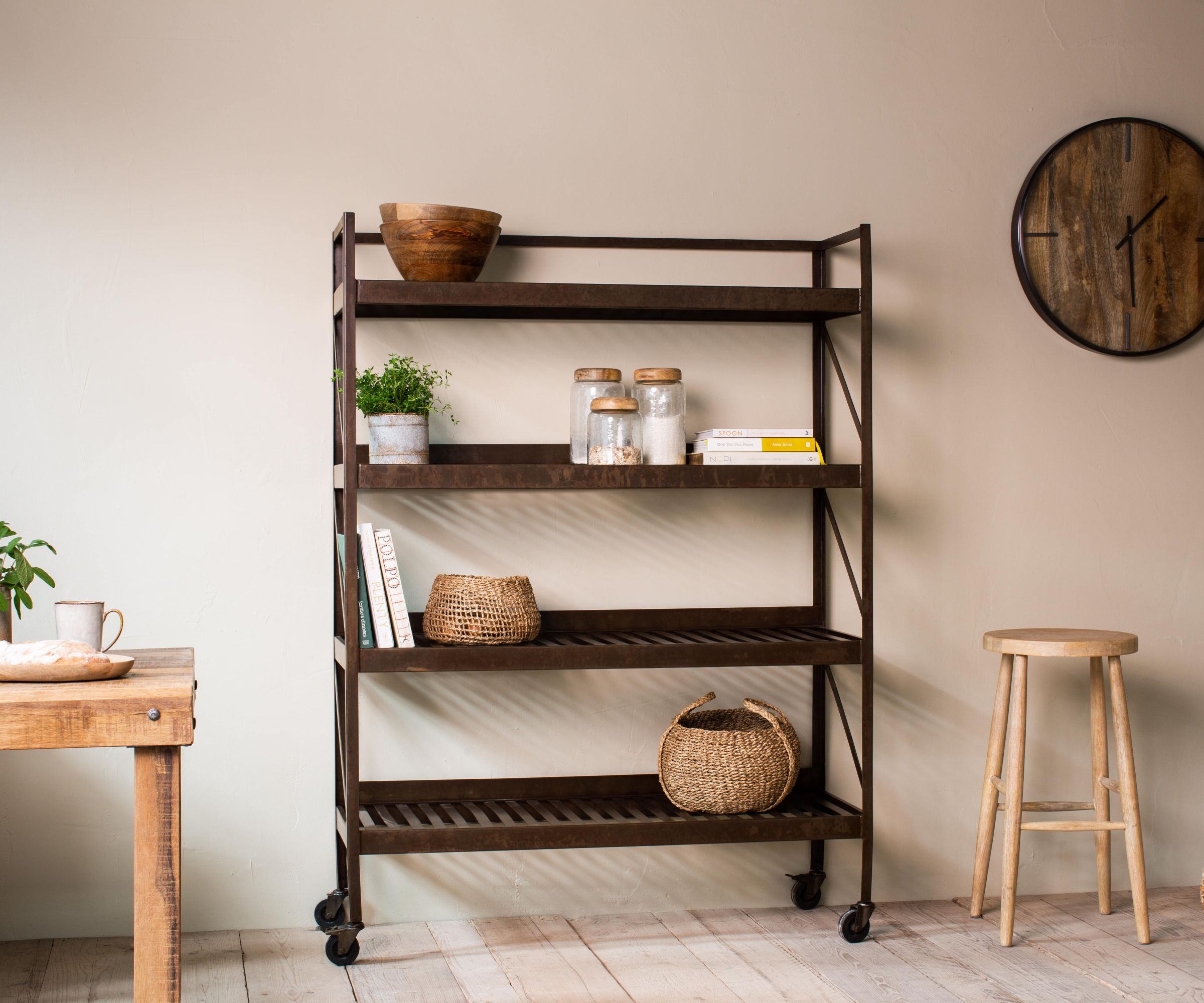 Metal-framed portable kitchen trolley with wooden shelves and castors, styled with jars, baskets and plants against a neutral wall.