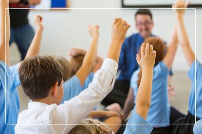 School children with back to camera with their hands up in class