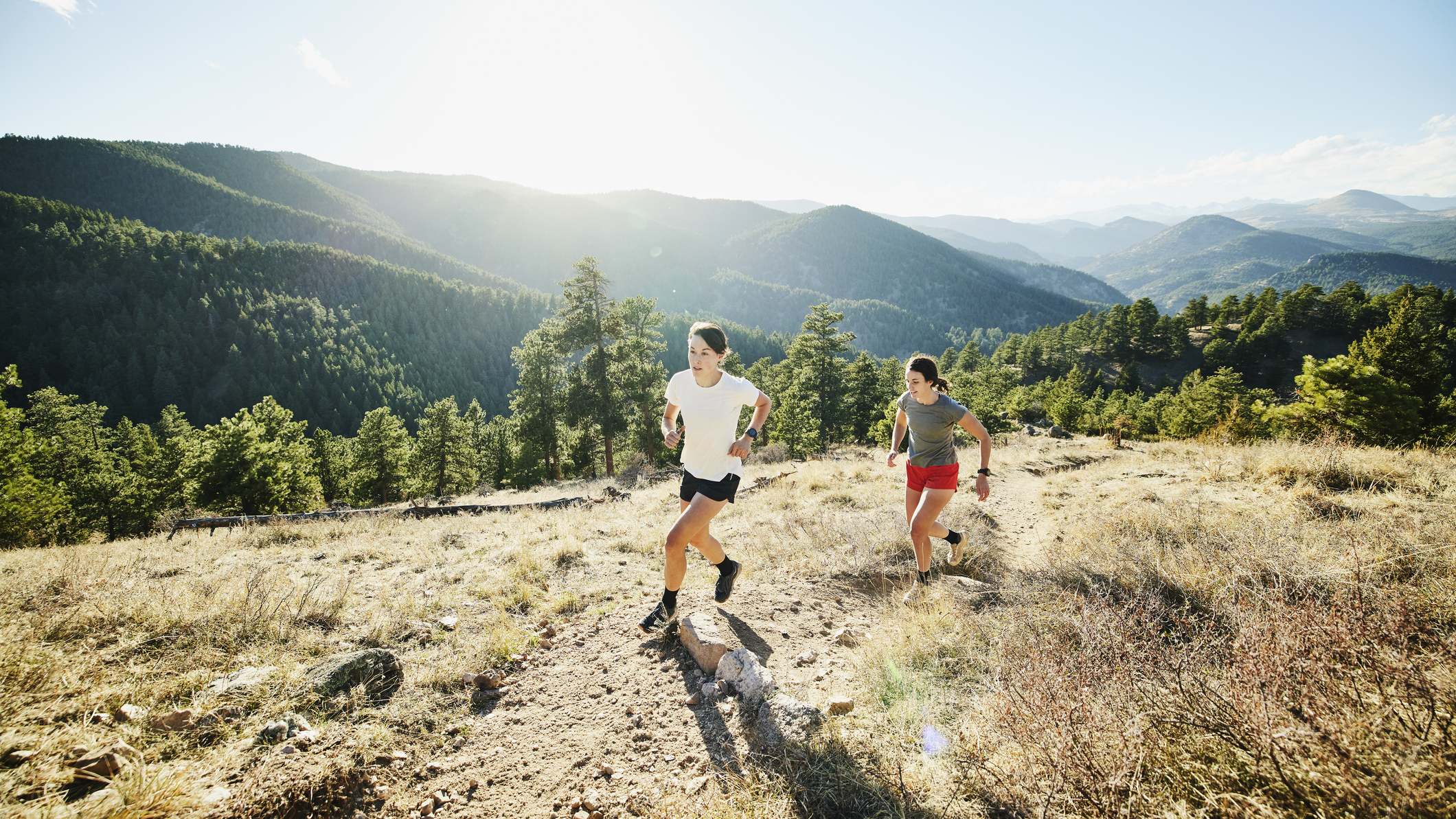 Two women running on a dirt tail with a vista of mountains behind them