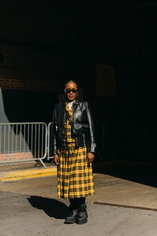 A Woman at fashion week wearing a flannels shirt outfit in yellow and a leather jacket.