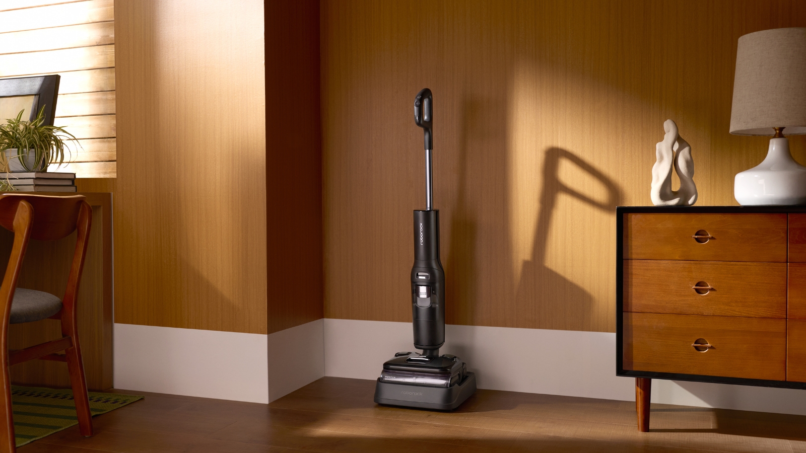 Roborock F25 Ultra vacuum-mop on charging base in brown room, pictured between wooden drawers and chair.