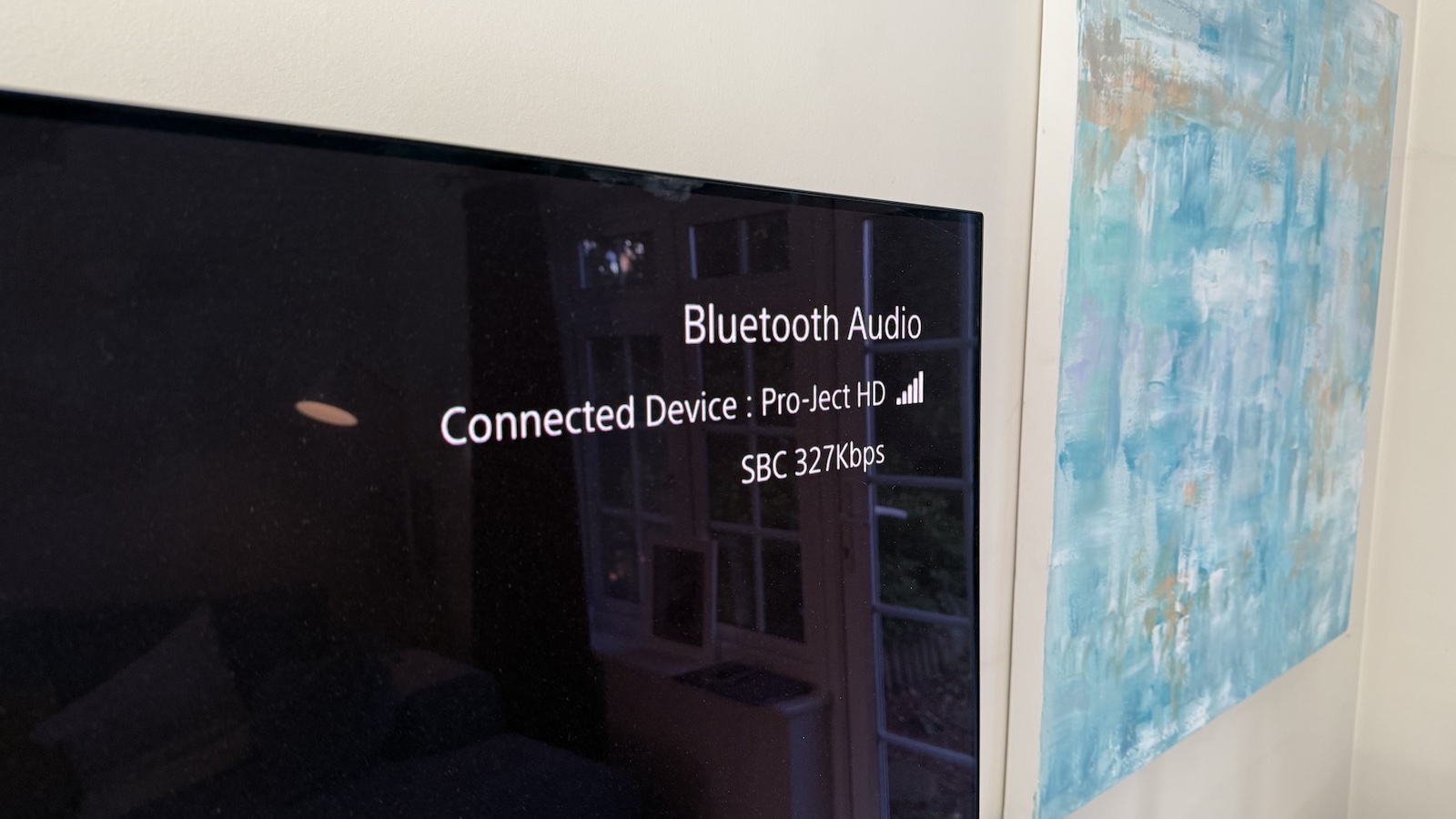 A TV displaying Bluetooth connected device next to a blue painting