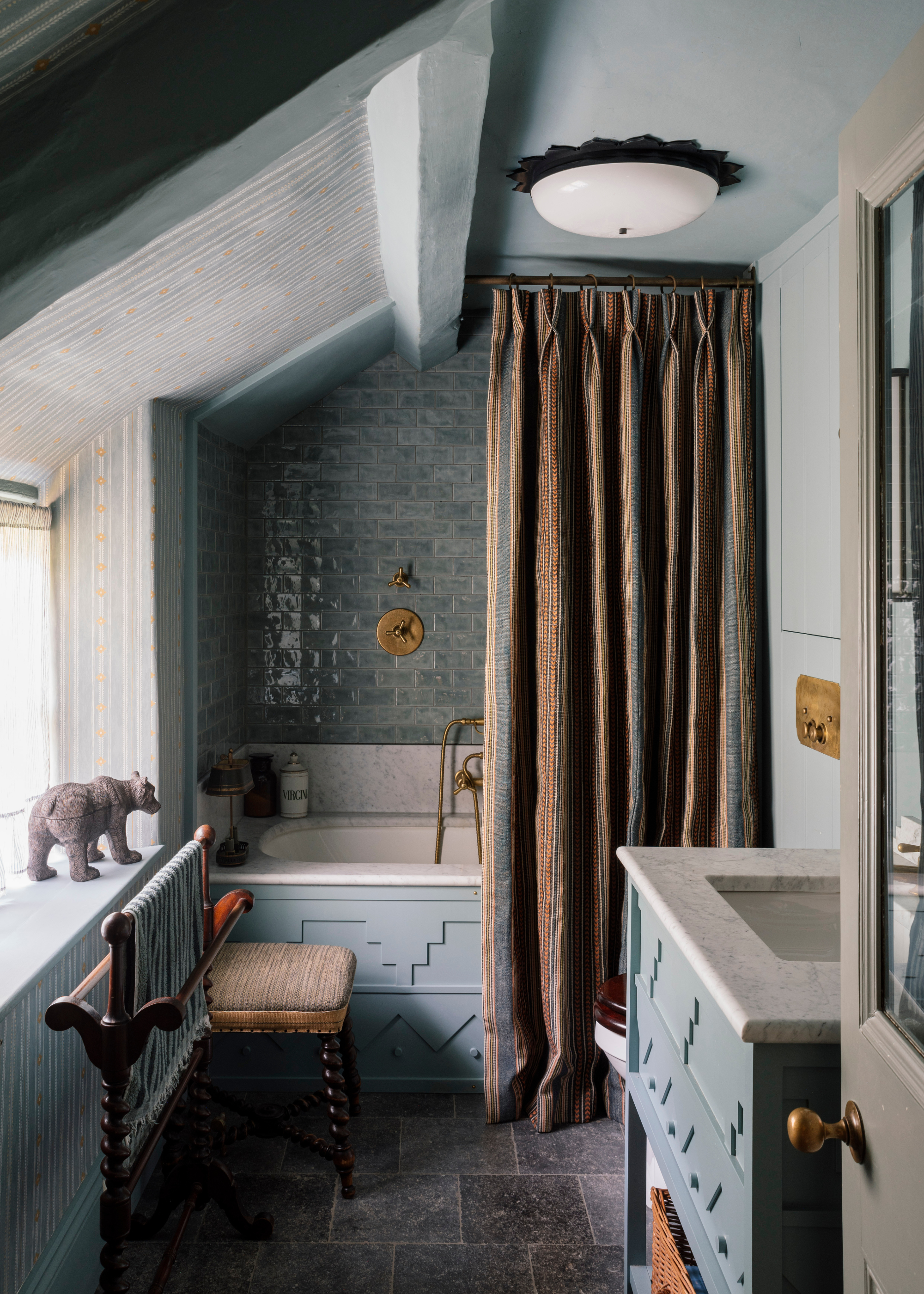 a pale blue zellige tiled bathroom with blue cabinetry and a dark earth tones shower curtain