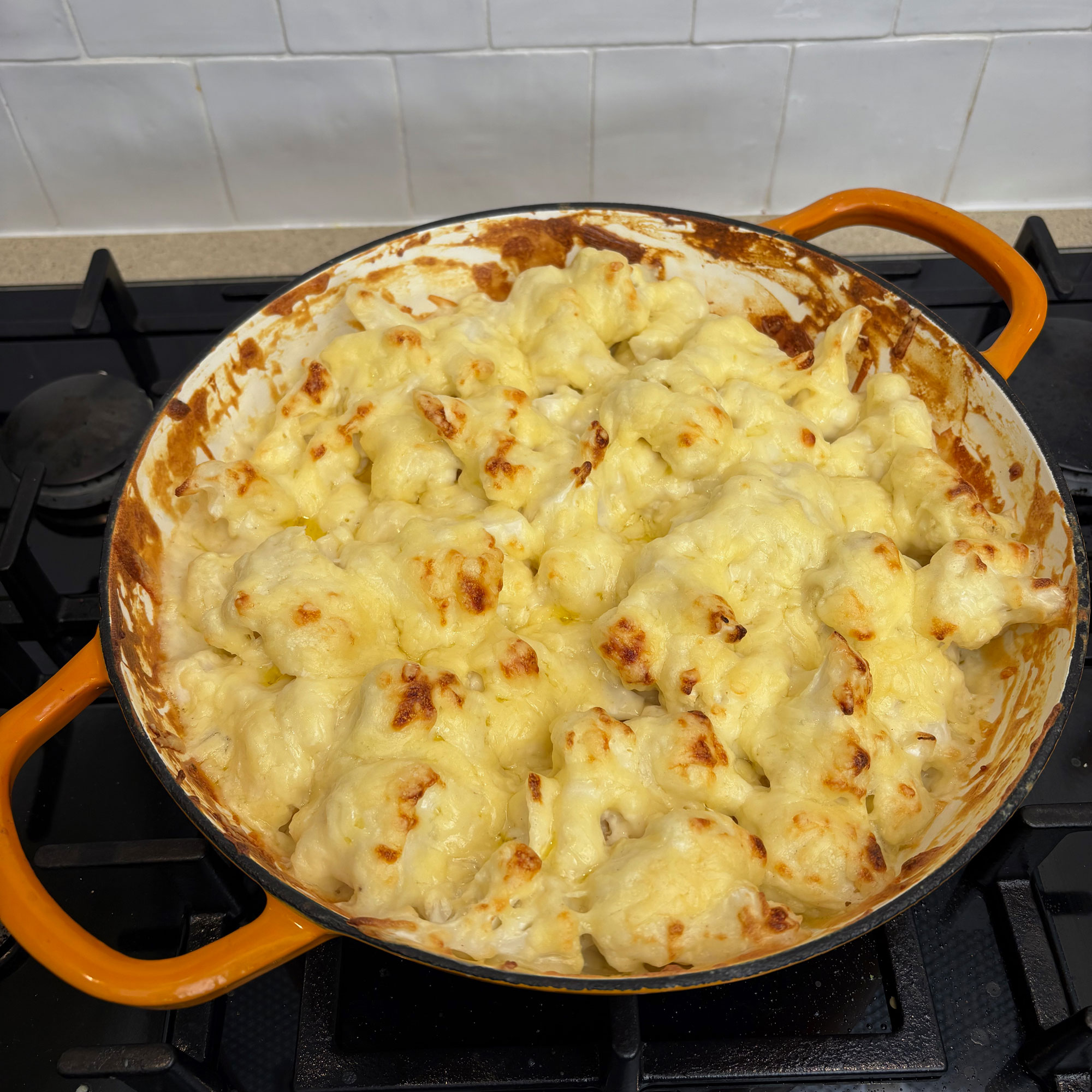 Orange cast iron pan on black hob with cauliflower cheese