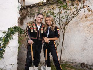 Alan Carr and Amanda Holden pose next to a wall with spades, next to an orange tree that they appear to have just planted. They are both wearing black boiler suits; Alan's is adorned with tassels to give him the look of a matador.