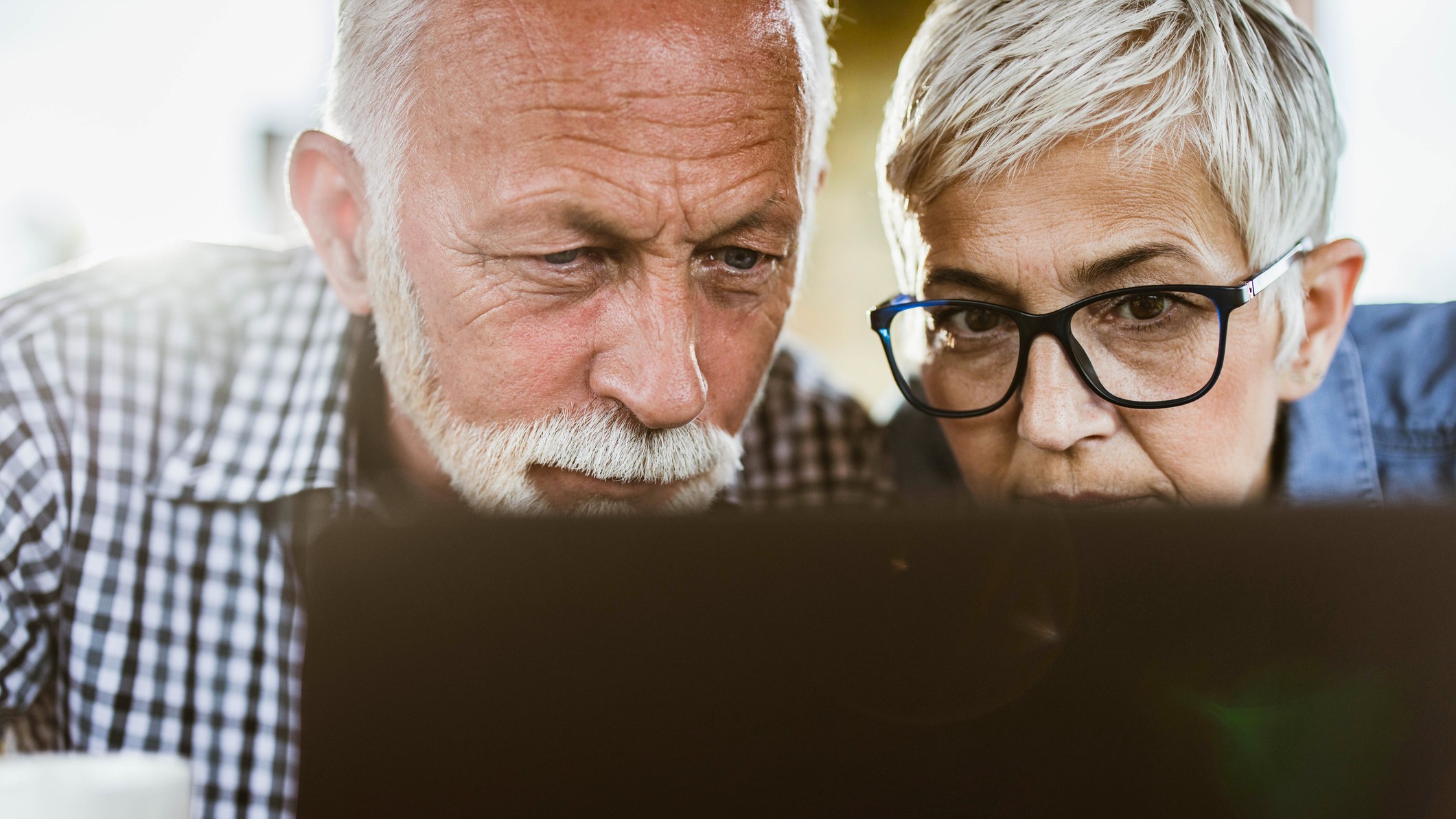 Mature couple with eyesight problems peering at a laptop.