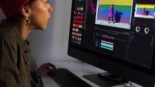Woman using Premiere Pro on a large monitor to edit video of a woman standing in front of a colourful garage door