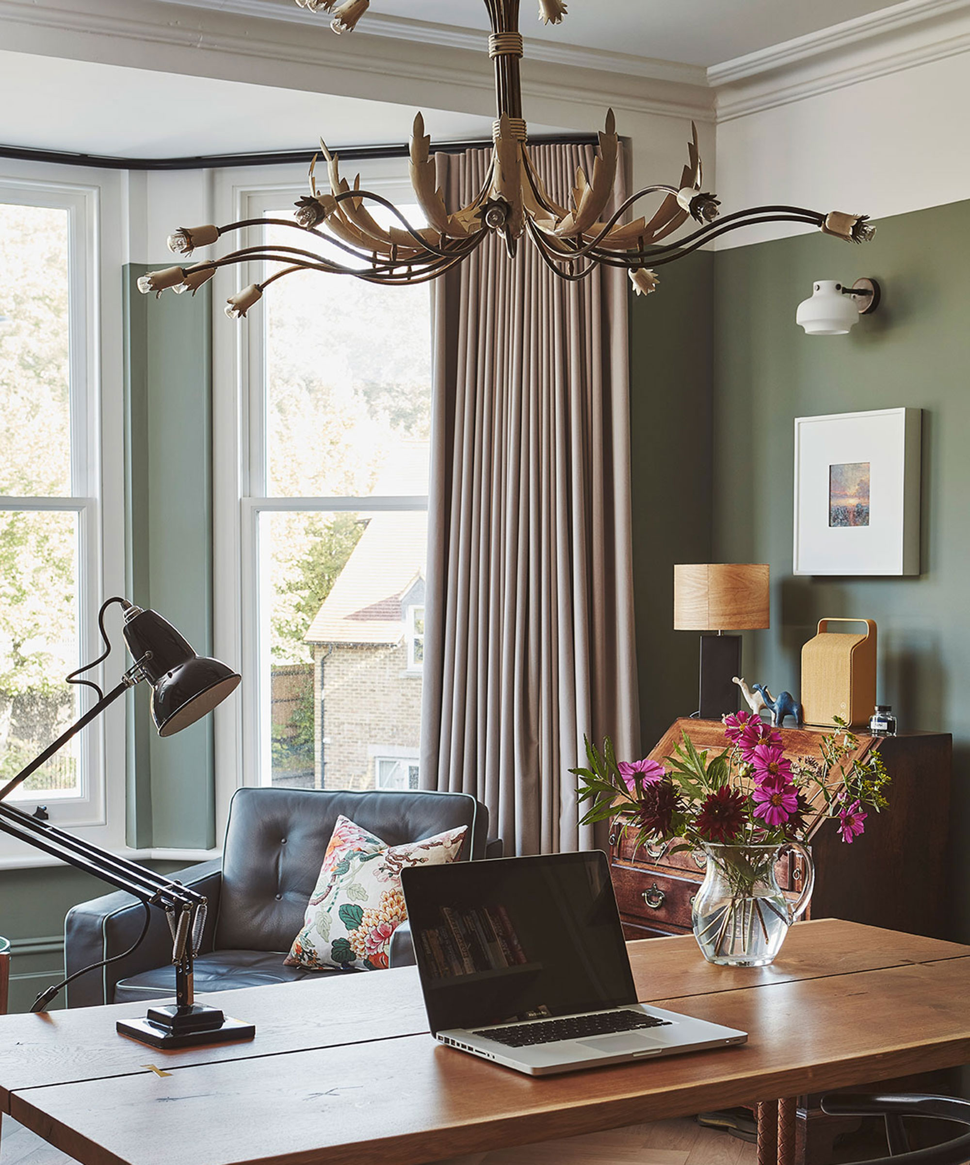 beautiful home office with large wooden desk and green walls and chandelier