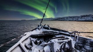 The nose of a fishing boat in the sea under the northern lights.