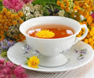 Tea in a white teacup and saucer surrounded by flowers