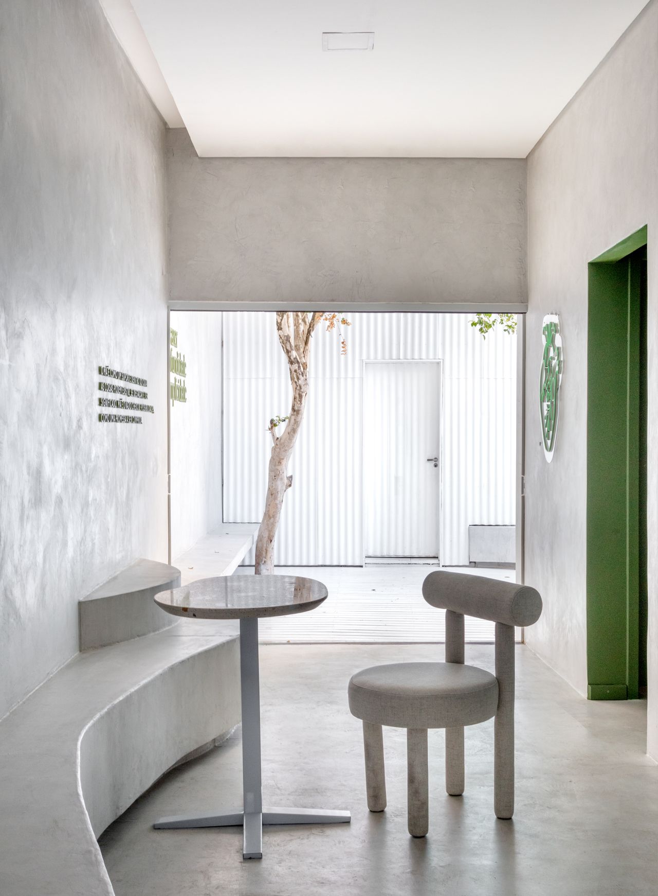 A white-washed, plastered matcha cafe with sculptural decor features monochromatic furnishings and an emerald green and chrome bar counter.