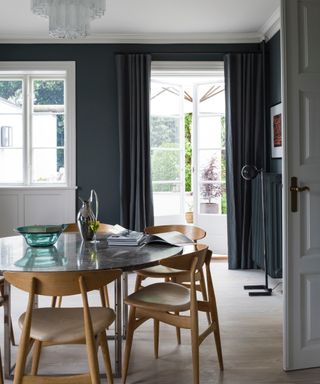 dining room painted in Farrow & Ball's Railings, white ceiling and woodwork, pale wood floor, retro chairs around black marble topped table black floor lamp, glassware